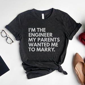 May include: A dark grey t-shirt with the text "I'm the engineer my parents wanted me to marry." printed in white.