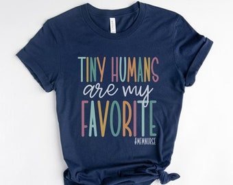 May include: A navy blue t-shirt with the text "Tiny Humans are my Favorite" in colorful letters. The text is in a playful font and the hashtag #MEMNURSE is printed below the text.