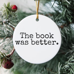 Puede incluir: Adorno navide&ntilde;o redondo blanco con texto negro que dice "El libro era mejor."