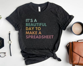 May include: A dark gray t-shirt with the text "It's a beautiful day to make a spreadsheet" in rainbow colors.