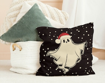 May include: A decorative pillow with a black background and white polka dots. The pillow features a cartoon ghost wearing a red Santa hat. Other pillows in a white basket are visible in the background.
