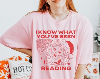 May include: Pink t-shirt with a red graphic of Santa Claus and the text "I know what you've been reading. Naughty List."
