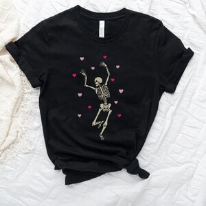 May include: Black t-shirt with a white skeleton dancing with pink hearts around it.