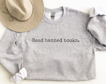 May include: Gray sweatshirt with the text "Read banned books." printed in black on the front. A brown fedora hat is lying on top of the sweatshirt.