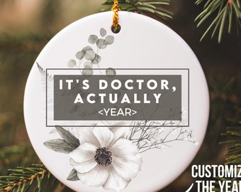 May include: White ceramic Christmas ornament with a floral design and the text "It's Doctor, Actually <YEAR>" with a customizable year.