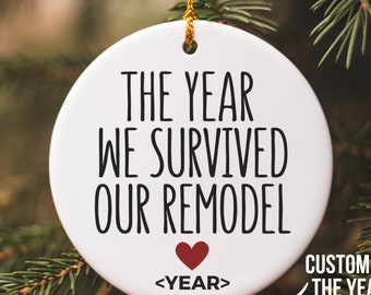 May include: White round ceramic ornament with black text that reads "The year we survived our remodel" with a red heart and the text "<YEAR>" below.  The ornament is hanging on a green Christmas tree branch.  Customize the year.