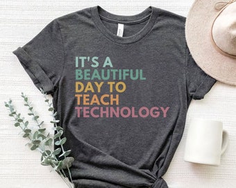 May include: A dark gray t-shirt with the text "It's a beautiful day to teach technology" in rainbow colors.