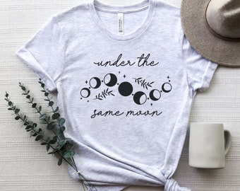 Puede incluir: Una camiseta gris claro con el texto "under the same moon" y un gráfico de una luna creciente y estrellas.