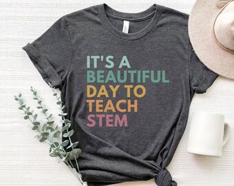 May include: A dark gray t-shirt with the text "It's a beautiful day to teach STEM" in rainbow colors.