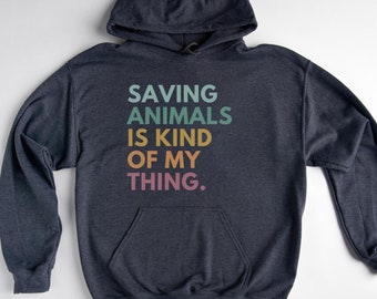Könnte beinhalten: Ein dunkelblauer Kapuzenpullover mit dem Text "SAVING ANIMALS IS KIND OF MY THING." in Regenbogenfarben.