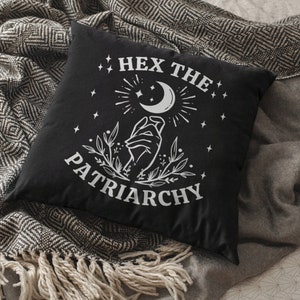 K&ouml;nnte beinhalten: Schwarzes Kissen mit wei&szlig;em Text, der "Hex the Patriarchy" lautet, und einer Grafik einer Hand, die einen Halbmond mit Sternen h&auml;lt.