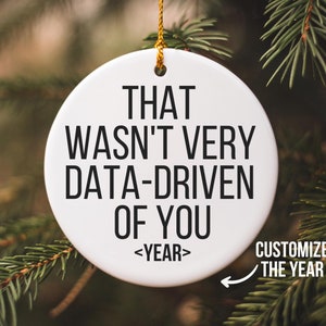 May include: White ceramic Christmas bauble with black text that reads "That wasn't very data-driven of you <YEAR>" with a gold string for hanging. You can customise the year.