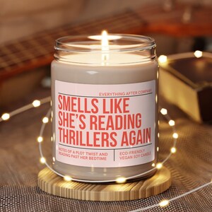 May include: A beige soy candle with a white label that reads "Smells Like She's Reading Thrillers Again". The label also includes the text "Everything After Company", "Notes of a plot twist and reading past her bedtime", and "Eco-friendly vegan soy candle".