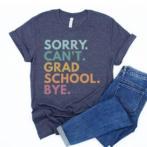 May include: A navy blue t-shirt with the text "SORRY. CAN'T. GRAD SCHOOL. BYE." in rainbow colors.