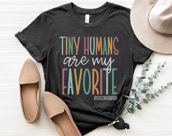 Peut inclure: Un t-shirt gris foncé avec le texte "Tiny Humans are my Favorite" en lettres colorées. Le texte est dans une police de caractères ludique et comprend le hashtag #PDGSONOGRAPHER.