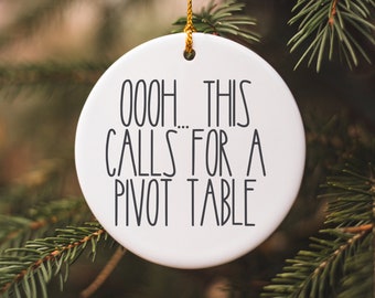 May include: A white, circular Christmas decoration with the words "OOOH... THIS CALLS FOR A PIVOT TABLE" in black. It is suspended by a gold string against a background of green fir needles.