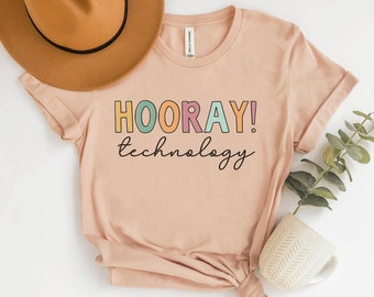 May include: A peach-colored t-shirt with the text "HOORAY! technology" in colorful letters. The letters are outlined in black and have a retro, playful style.