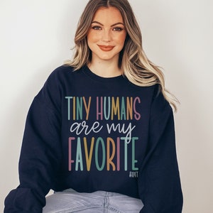 May include: A navy blue sweatshirt with the text "TINY HUMANS are my FAVORITE" in colorful letters. The text is in a playful, handwritten font.