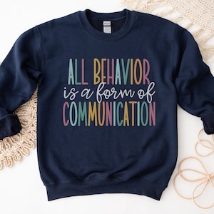 May include: Navy blue sweatshirt with the text "ALL BEHAVIOR is a form of COMMUNICATION" in colourful letters.