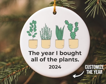 May include: White ceramic Christmas ornament with a green and yellow illustration of potted plants. The text reads "The year I bought all of the plants. 2024" with an arrow pointing to the year and the text "Customize the year".