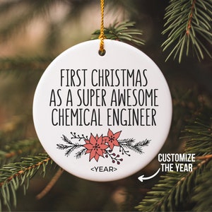 May include: A white ceramic Christmas ornament with the text "FIRST CHRISTMAS AS A SUPER AWESOME CHEMICAL ENGINEER". The ornament has a floral design and a gold string for hanging. The text "CUSTOMIZE THE YEAR" is also present.