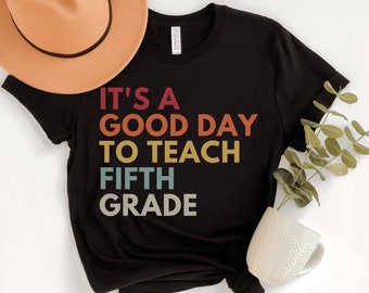May include: Black t-shirt with a vintage-style graphic that reads "It's a good day to teach fifth grade".