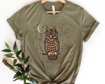 May include: A green t-shirt with a graphic of an owl perched on a branch with a crescent moon and stars in the background.