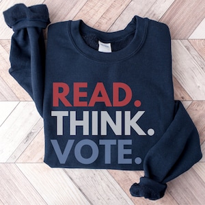 May include: Navy blue sweatshirt with the words "READ. THINK. VOTE." in red, gray, and blue. The sweatshirt is made of a soft material and has a crew neck. The text is centered on the front of the garment.