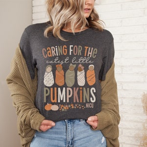 May include: A dark gray t-shirt with the text "Caring for the cutest little pumpkins" and a graphic of five babies wrapped in blankets. The text "NICU" is also on the shirt.