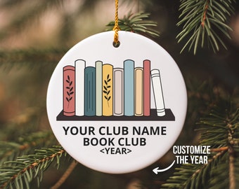 Peut inclure: Ornement en céramique blanche avec une illustration colorée d'une bibliothèque avec des livres. Le texte indique "Your Club Name Book Club <YEAR>" avec une flèche pointant vers l'année, indiquant qu'elle est personnalisable.