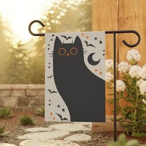 May include: A black cat with orange eyes and a crescent moon behind it. The cat is surrounded by bats and stars on a white background. The image is a garden flag.