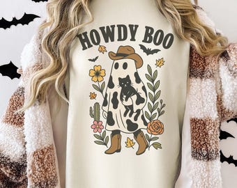 May include: Cream-colored sweatshirt with the text "HOWDY BOO" above a ghost wearing a cowboy hat and boots, holding a black cat. The ghost is decorated with black spots and surrounded by floral and leaf illustrations.