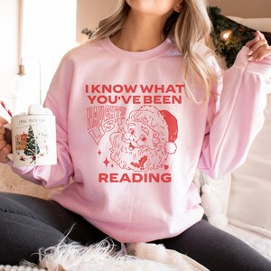 May include: Pink Christmas sweatshirt with a red graphic of Santa Claus and the text "I know what you've been reading. Naughty List."