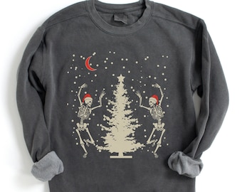 May include: A dark gray sweatshirt with a festive design featuring two skeletons dancing in front of a Christmas tree. The skeletons are wearing Santa hats and the tree is decorated with a star.