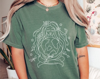 May include: A green t-shirt with a white outline of a woman holding the earth. The woman has flowers in her hair and there are stars and dragonflies around her.