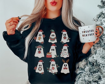 May include: Black sweatshirt with a Christmas ghost design. The ghosts are wearing Santa hats, elf hats, reindeer antlers, and other festive accessories. The text "Sweater Weather" is on a white mug.
