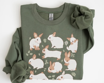 May include: A green sweatshirt with a pattern of white rabbits with brown ears and noses. The rabbits are surrounded by small green leaves.