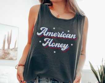 May include: A dark gray tank top with the text "American Honey" in a retro font with red, white, and blue accents. The text is surrounded by white stars.