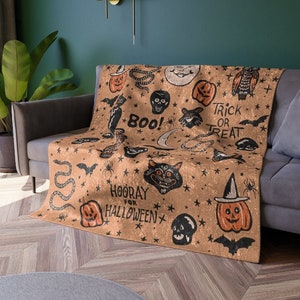 May include: A brown throw blanket with a Halloween theme. It features a variety of spooky and fun designs, including pumpkins, bats, cats, snakes, and stars. The text "Boo!" and "Hooray for Halloween" are printed on the blanket.