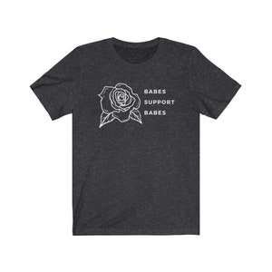 May include: A dark heather grey t-shirt with a white outline of a rose and the text "BABES SUPPORT BABES".