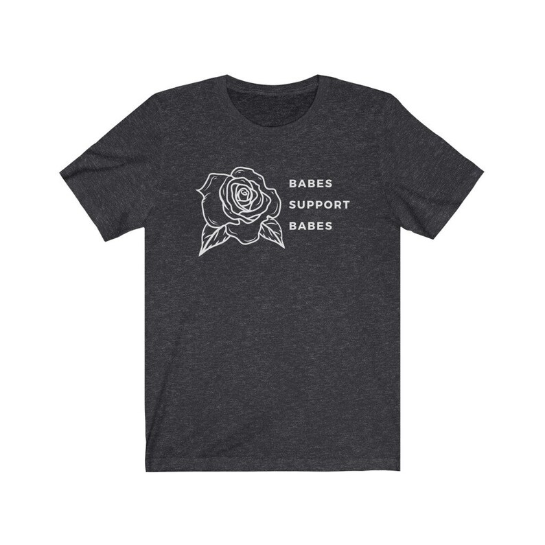 May include: A dark heather grey t-shirt with a white outline of a rose and the text "BABES SUPPORT BABES".