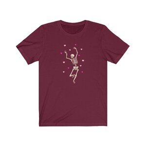 May include: A maroon t-shirt with a white skeleton dancing and pink hearts scattered around it.