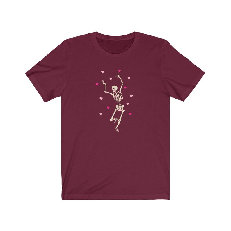 May include: A maroon t-shirt with a white skeleton dancing and pink hearts scattered around it.