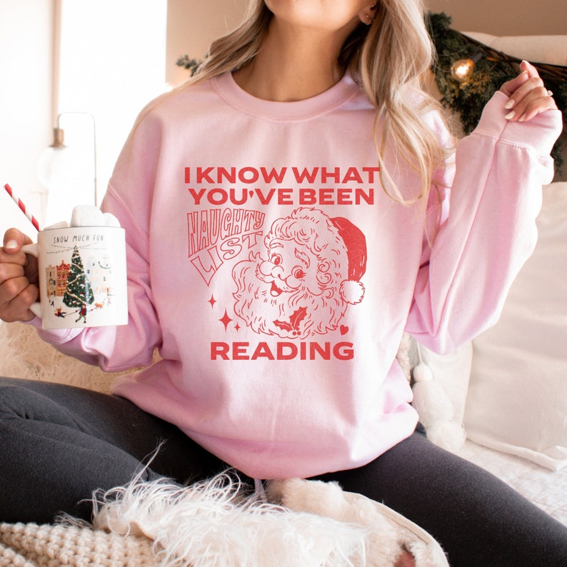 May include: Pink Christmas sweatshirt with a red graphic of Santa Claus and the text "I know what you've been reading. Naughty List."