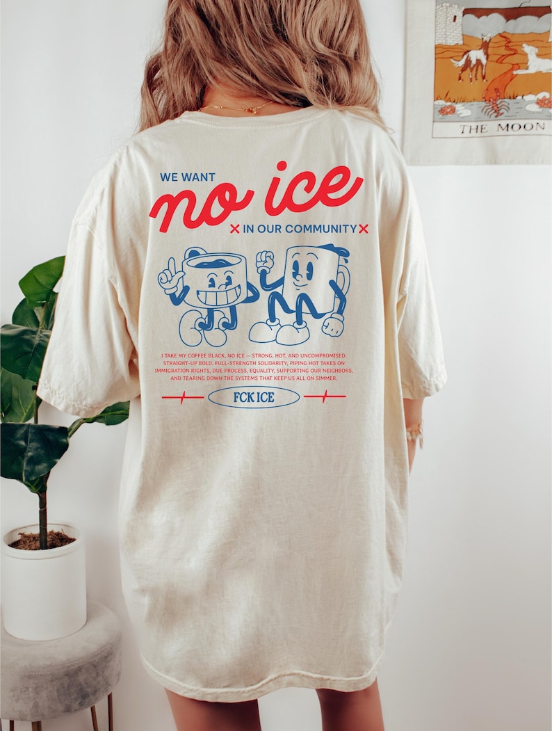 Op de afbeelding: Cr&egrave;mekleurig T-shirt met de tekst "WE WANT no ice IN OUR COMMUNITY" in rood en blauw. De achterkant van het shirt heeft cartoon koffiekopjes en extra tekst. Het shirt heeft ook de tekst "FCK ICE".