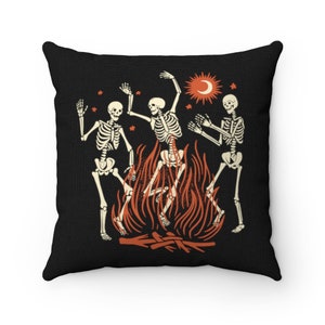 May include: Three skeletons dancing around a campfire with flames in orange and red. The skeletons are white with black outlines. The background is black with white stars and a sun and moon in the top right corner.