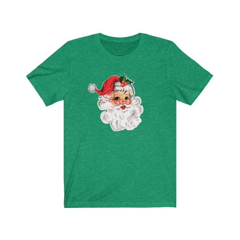 May include: A green t-shirt with a vintage illustration of Santa Claus's face. The illustration is in a cartoon style with a red hat, white beard, and rosy cheeks.