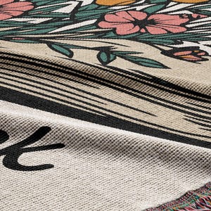 Peut inclure: Une couverture en tapisserie tiss&eacute;e avec un motif floral et un livre avec le texte "Read" dessus. La couverture a une bordure en franges.