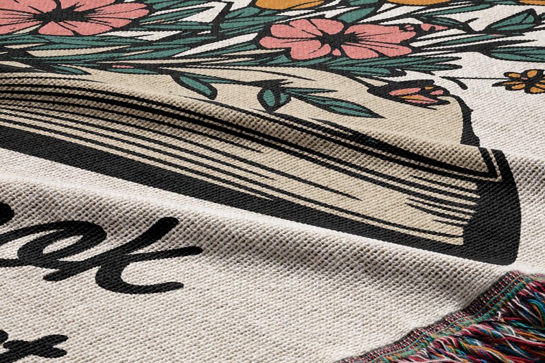 Peut inclure: Une couverture en tapisserie tiss&eacute;e avec un motif floral et un livre avec le texte "Read" dessus. La couverture a une bordure en franges.