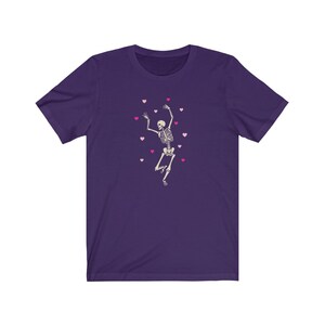 May include: Purple t-shirt with a white skeleton dancing and pink hearts scattered around it.
